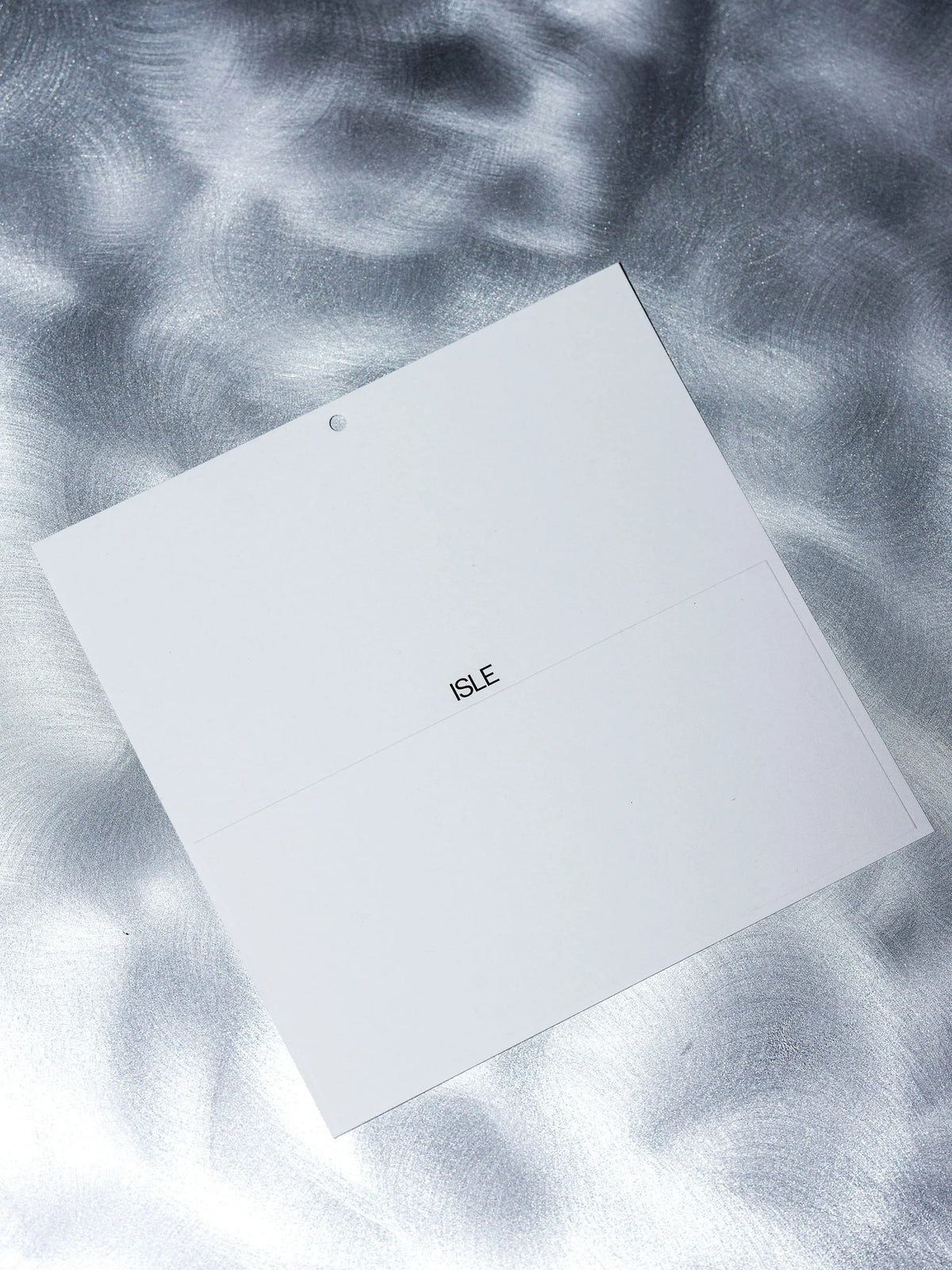 ISLE — carton blanc estampé du logo posé sur surface aux reflets d'eau