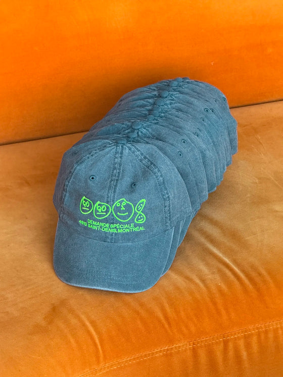 Pile de casquettes bleu-vertes Demande Spéciale sur un fauteuil orange