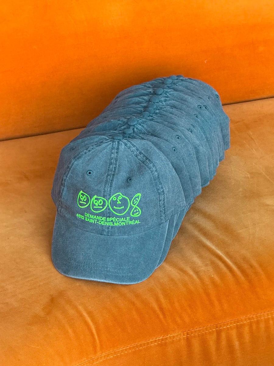 Pile de casquettes bleu-vertes Demande Spéciale sur un fauteuil orange