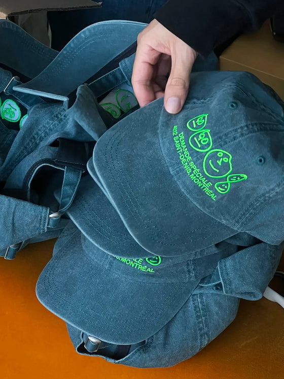 Main tenant la casquette bleu-verte Demande Spéciale au-dessus d'une veste en jean