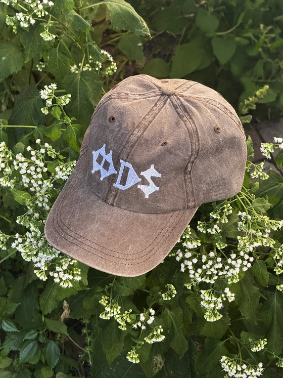 Casquette kaki délavée à logo OODS brodé blanc, posée dans la verdure