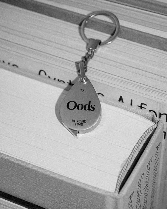 Porte-clé loupe « Oods » accroché à un livre ouvert, photo noir et blanc