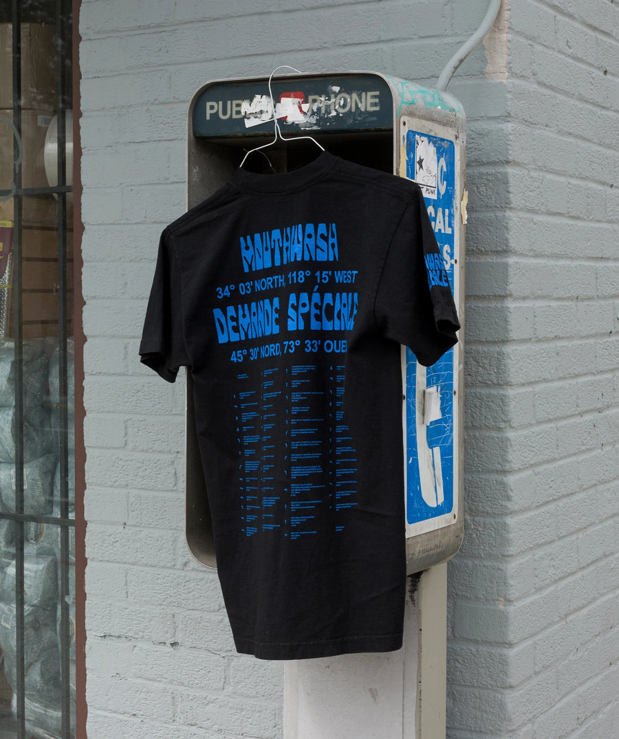 T-shirt noir, dos imprimé en bleu, accroché à une cabine téléphonique