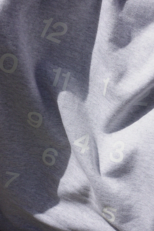 Gros plan du tissu gris chiné, broderie ton sur ton des chiffres d'une horloge (OODTIMES)