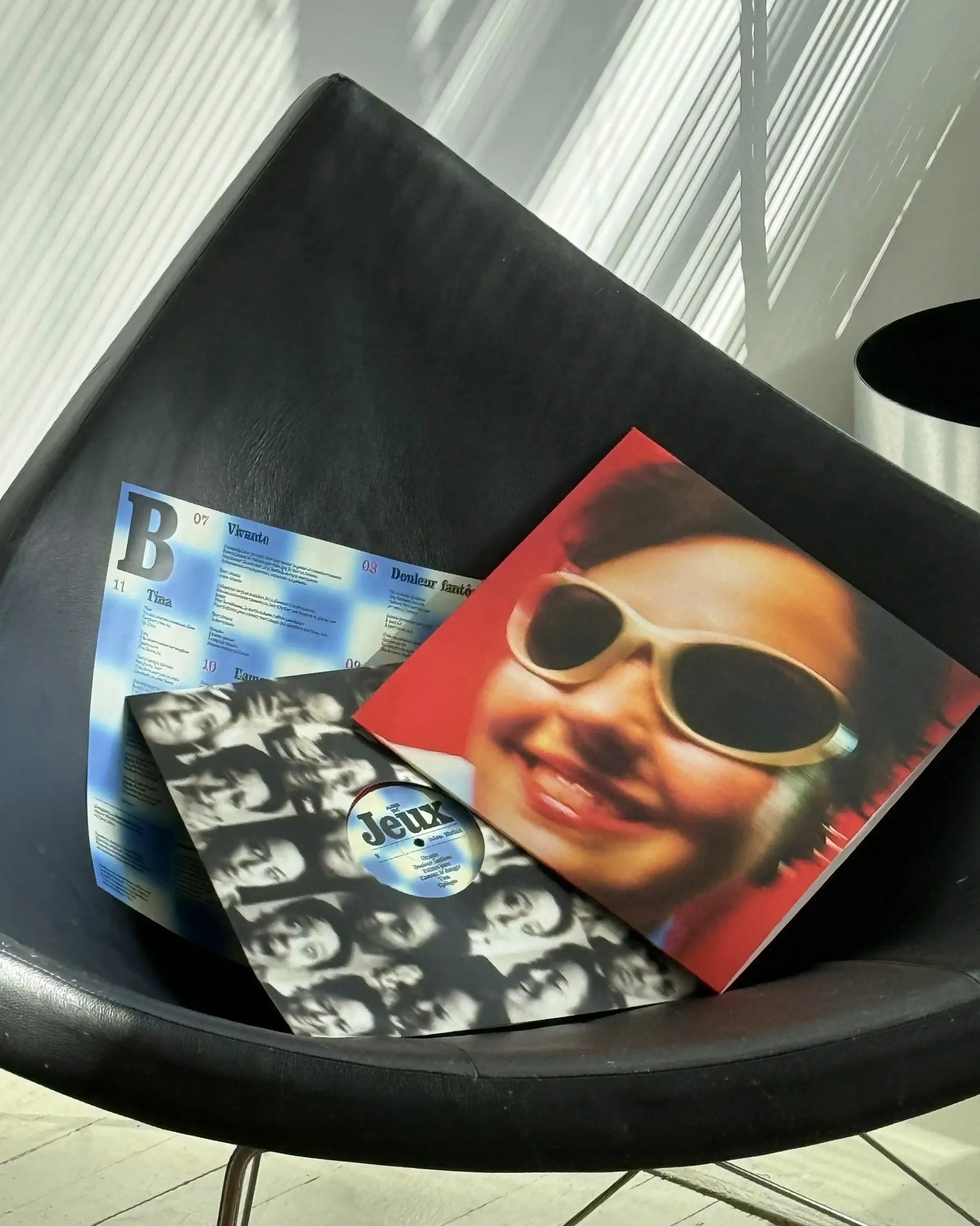 Airs de Jeux — deux pochettes vinyles sur une chaise design, recto à lunettes blanches et verso damier