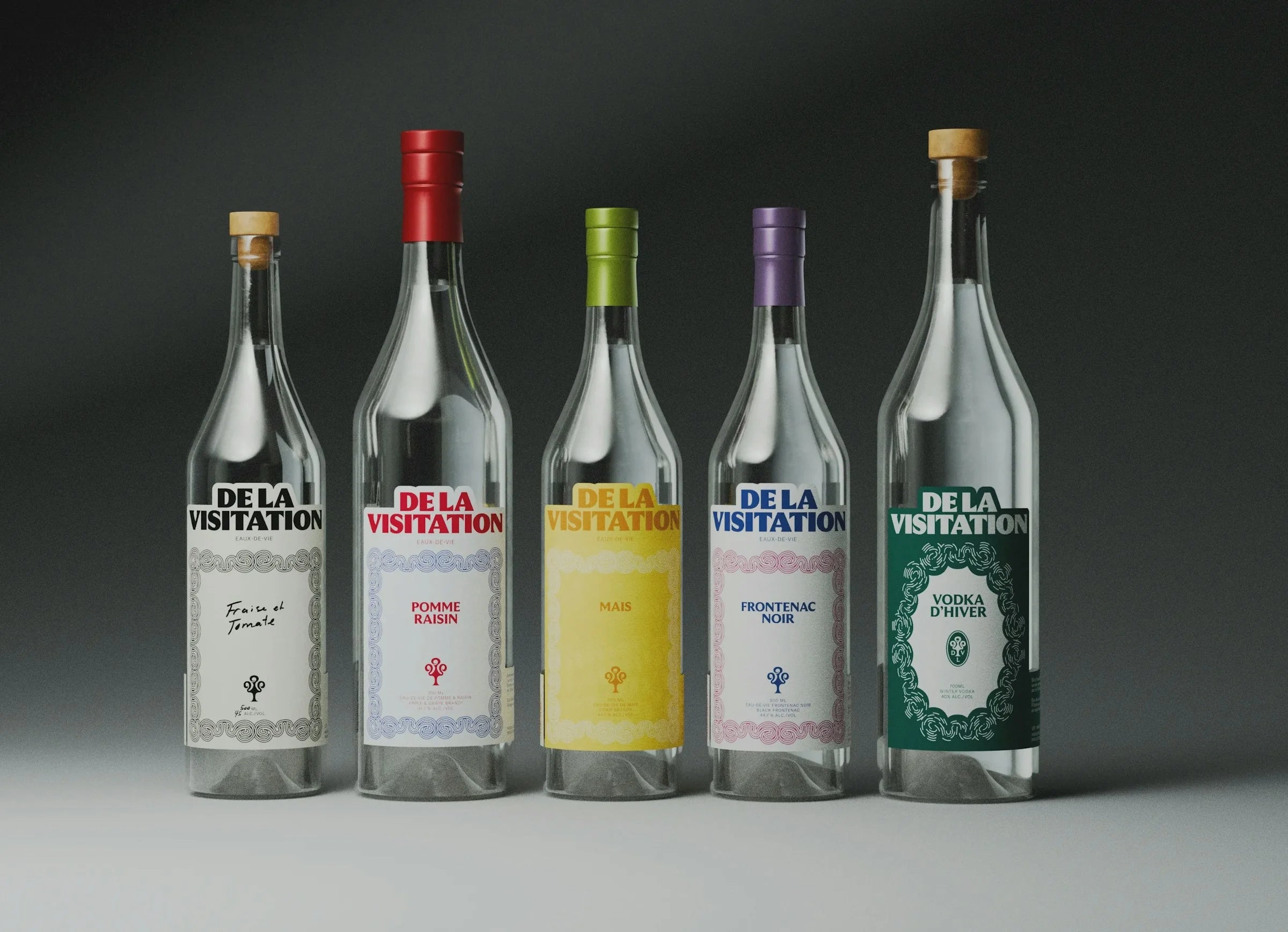 De la Visitation — gamme de cinq bouteilles d'eaux-de-vie aux étiquettes colorées, fond gris studio