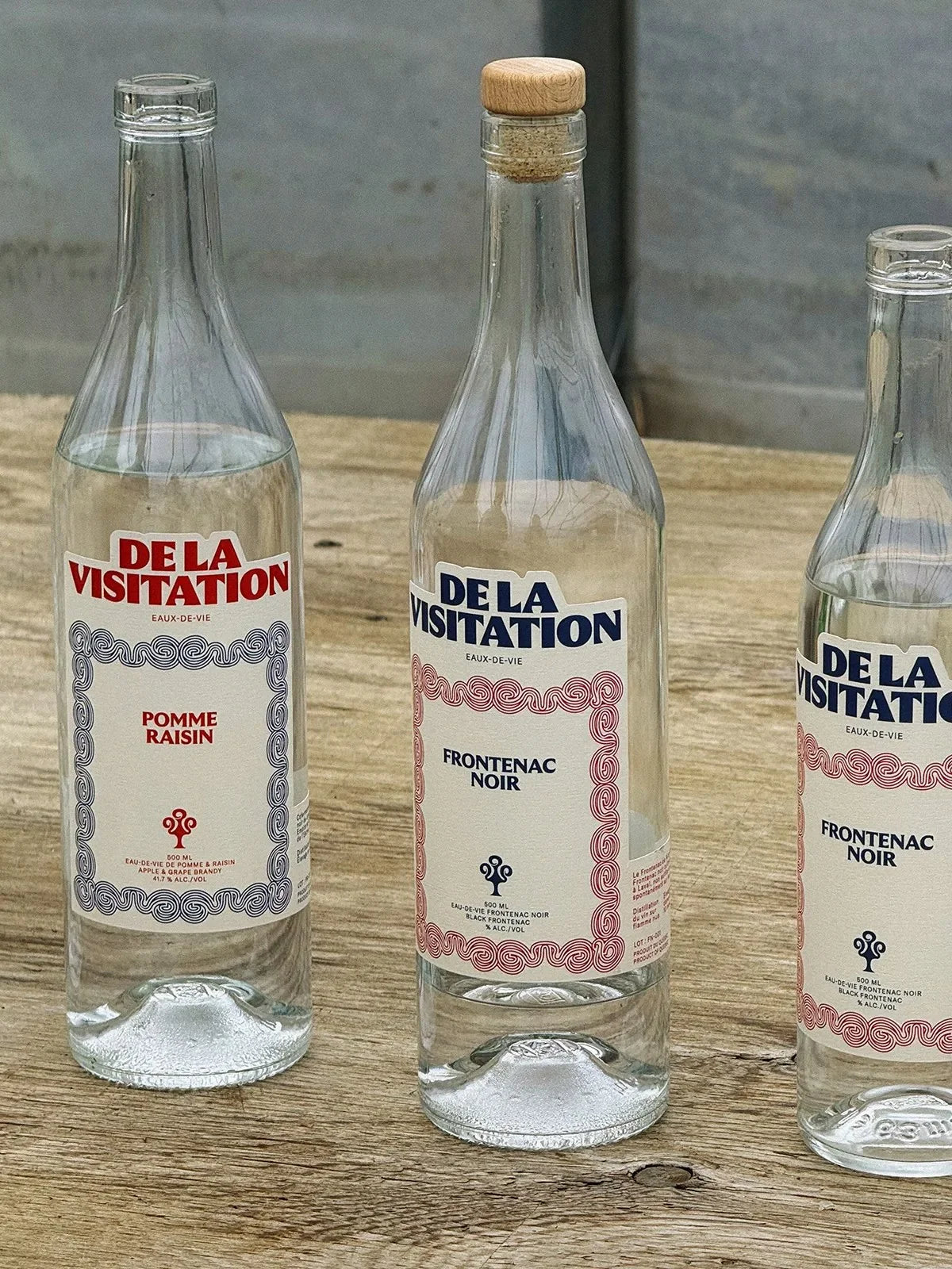De la Visitation — trois bouteilles aux étiquettes pastel alignées sur une table
