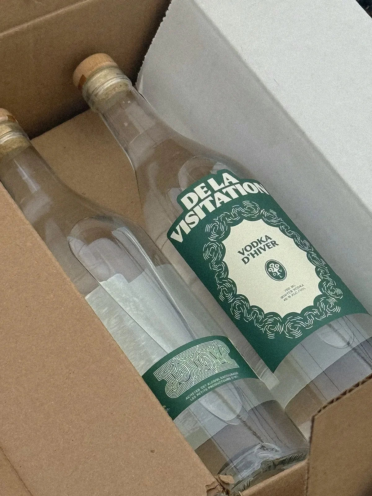 De la Visitation — deux bouteilles à étiquettes vertes dans une boîte de carton ouverte