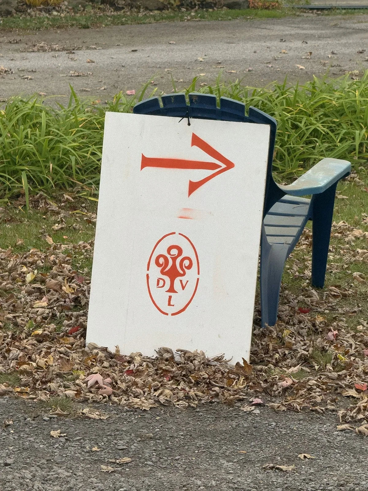 De la Visitation — panneau directionnel blanc à flèche et logo orange posé sur une chaise en bord de chemin