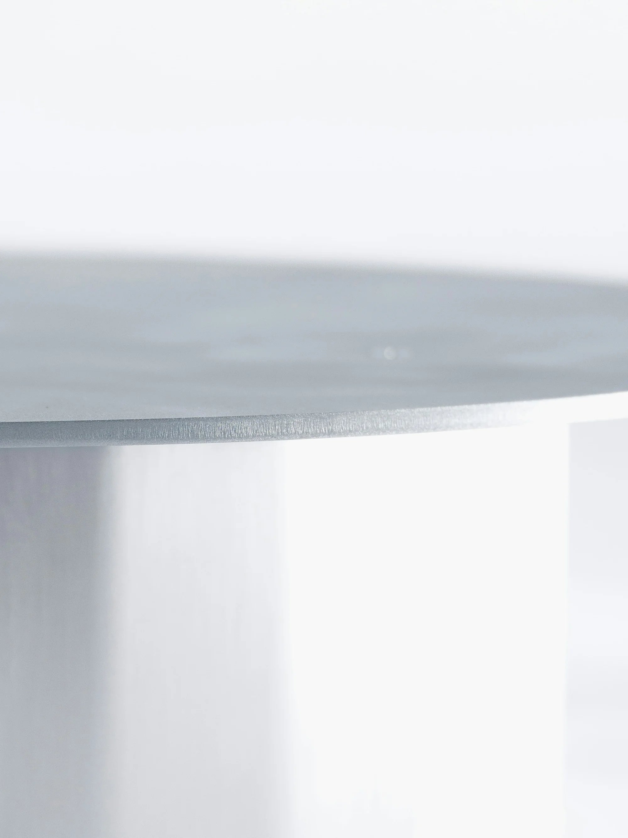 ISLE — détail d'une table ronde en métal brossé clair, gros plan sur le rebord