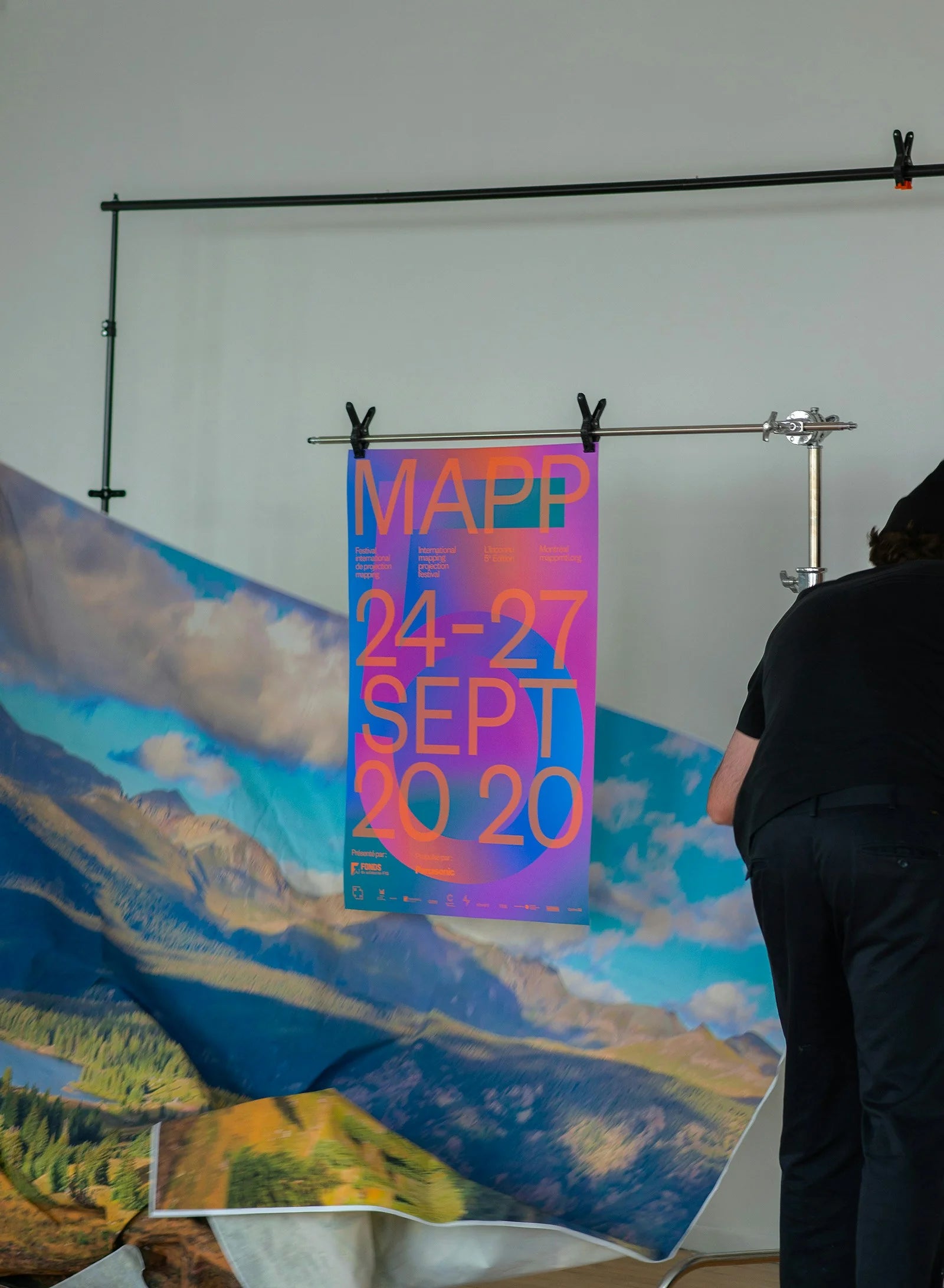 L'inconnu — maquette de l'affiche dégradée fuchsia accrochée en studio, près d'un paysage de montagnes imprimé