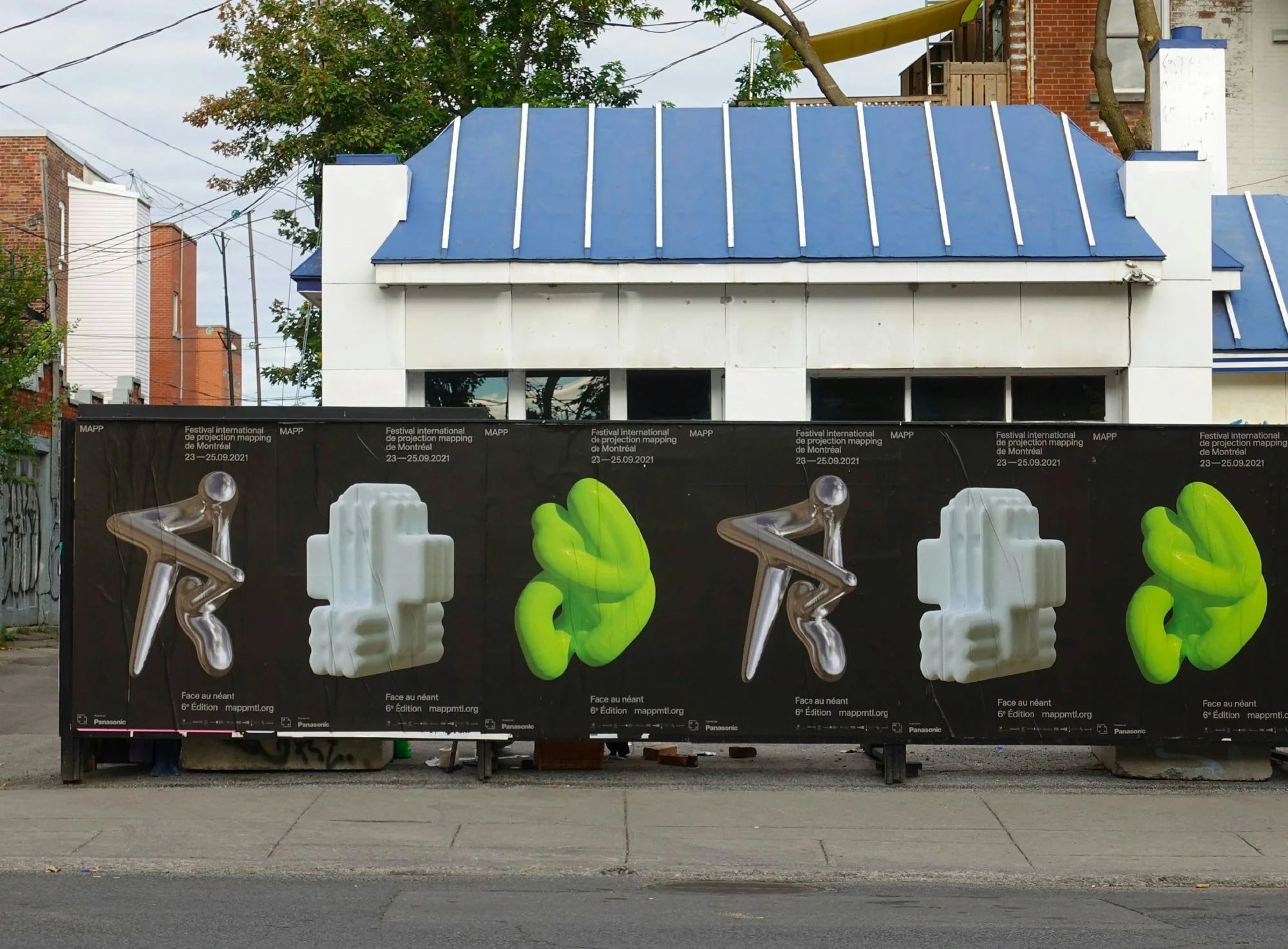 Face au néant — palissade de chantier extérieure tapissée des affiches argentées et vert fluo du festival