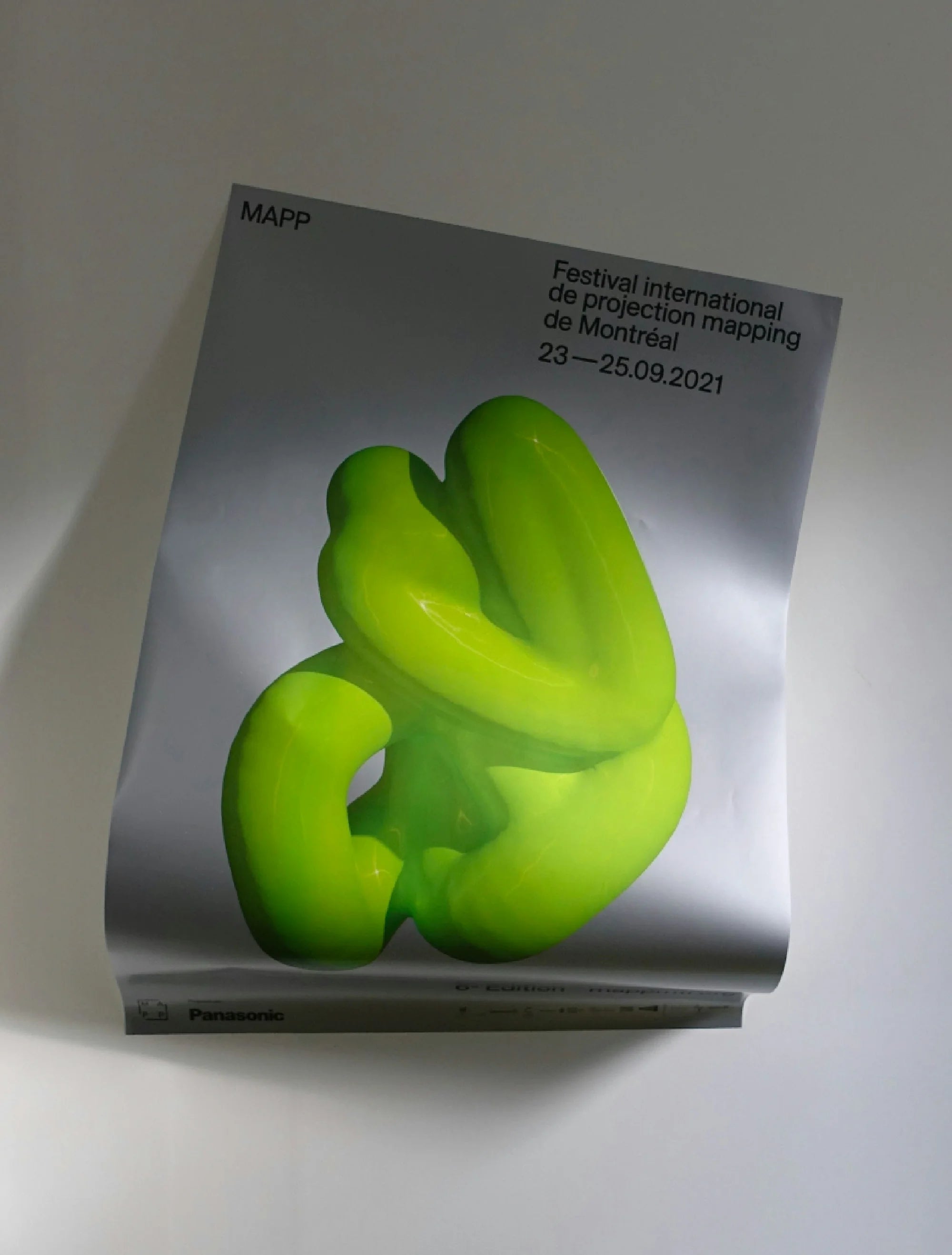 Face au néant — affiche argentée du festival avec sculpture 3D vert fluo, légèrement gondolée sur fond clair