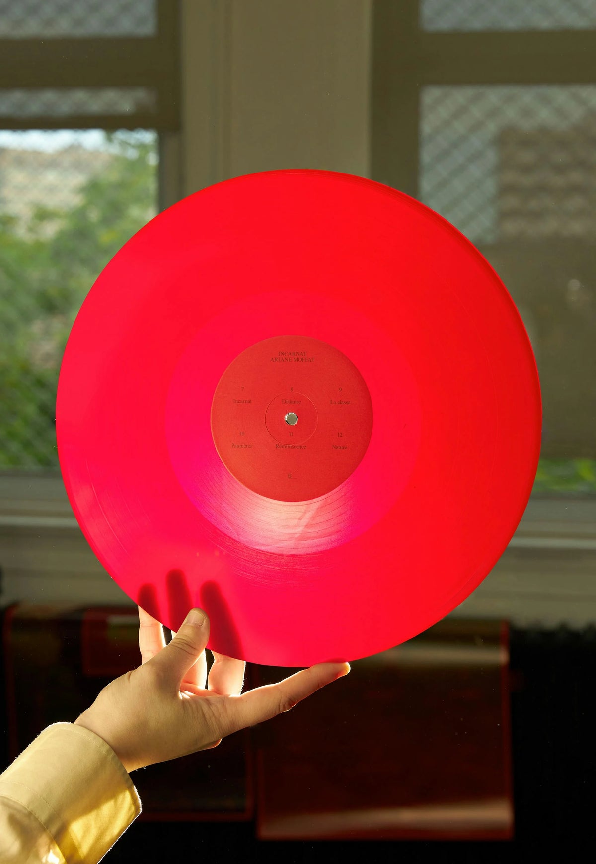 Ariane Moffatt — disque vinyle rouge translucide d'Ariane Moffatt tenu en main devant une fenêtre