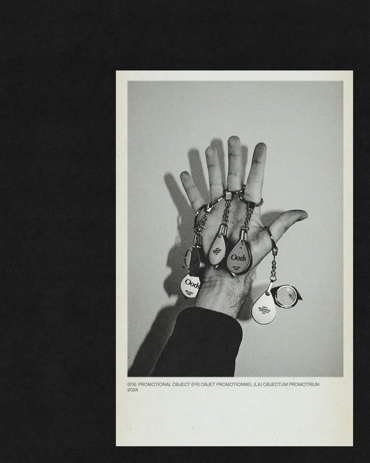 Beyond Time — main ouverte tenant des porte-clés et objets promotionnels, photo noir et blanc