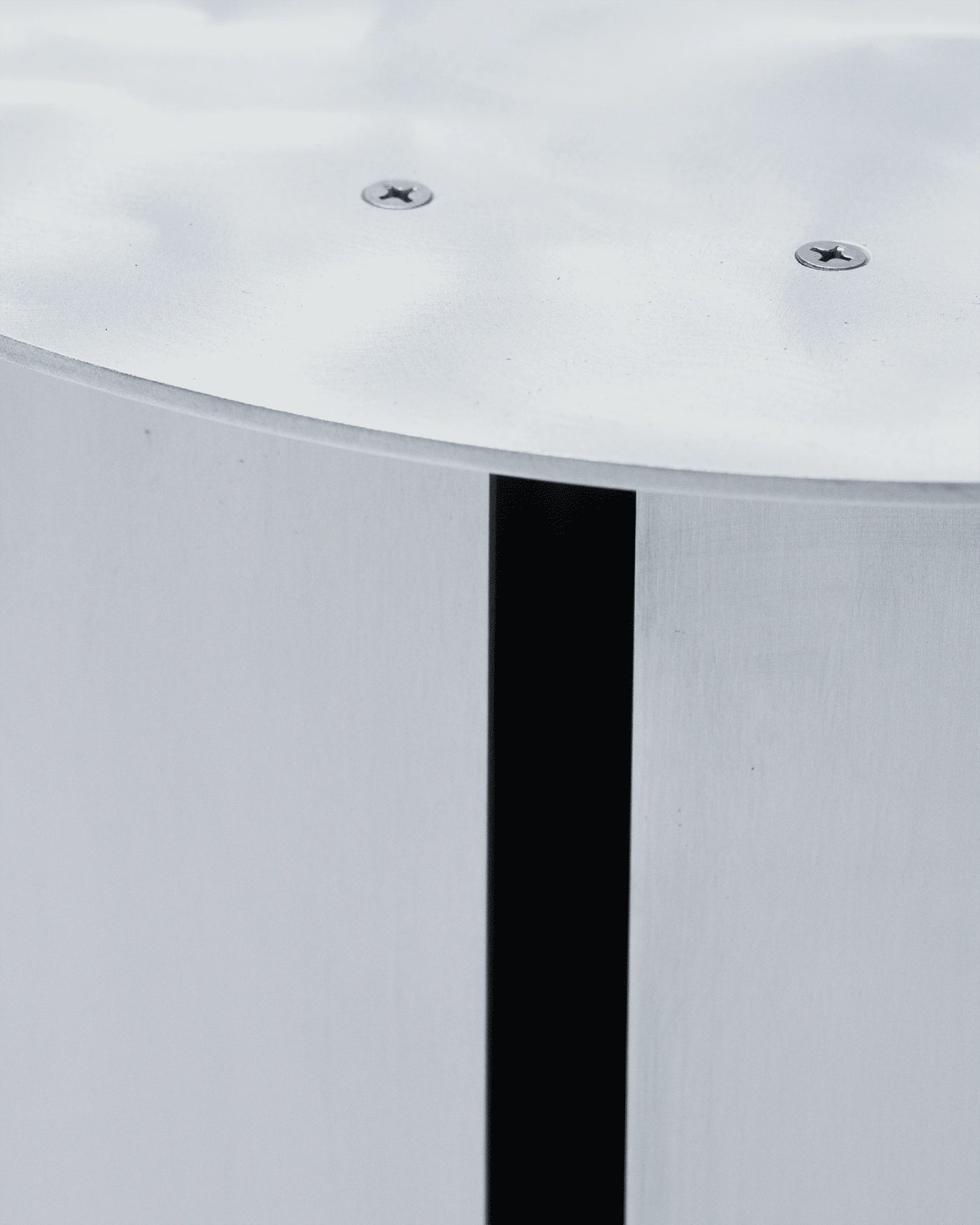 SANGARE — gros plan d'un tabouret cylindrique en métal brossé avec dessus vissé, sur fond gris clair