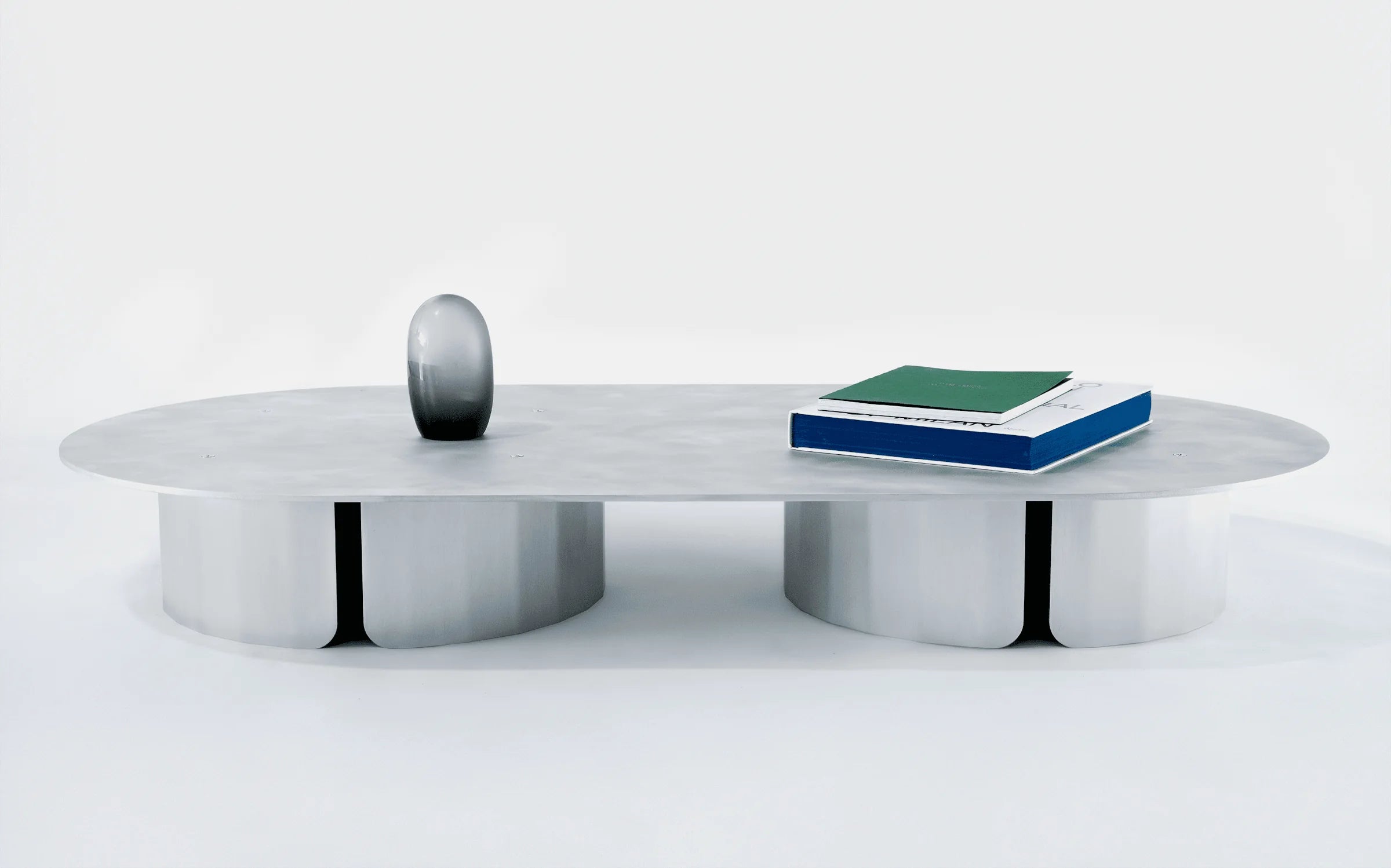 SANGARE — table basse ovale en aluminium poli avec deux livres et galet décoratif posés dessus
