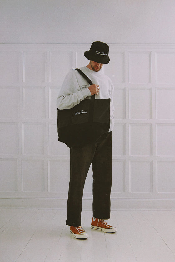 Personne debout, chapeau noir, portant le tote bag Office Of Demande Spéciale