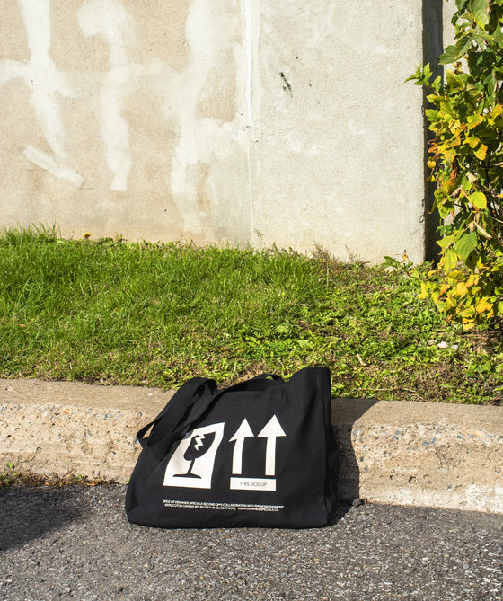 Tote bag Fragile Handle With Care posé sur un trottoir, devant un mur blanc