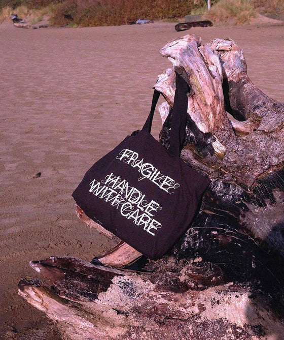 Tote bag Fragile Handle With Care posé sur un rocher, au bord de l'eau