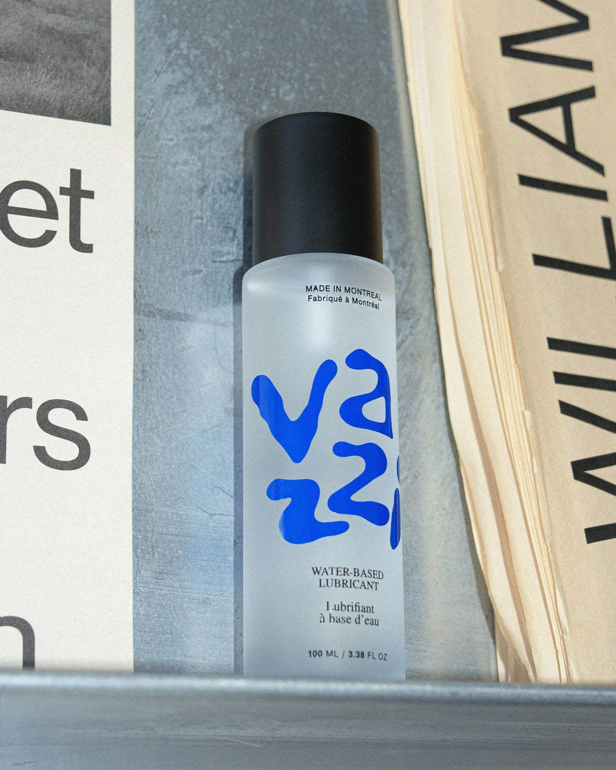 Vazzi — flacon givré de lubrifiant au logo bleu posé près de pages imprimées