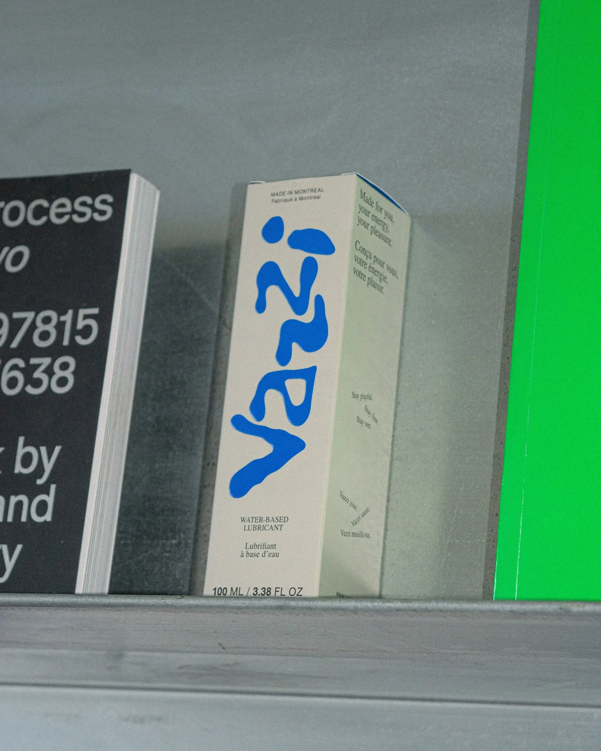 Vazzi — étui de lubrifiant au logo bleu posé sur une tablette devant affiches typographiques