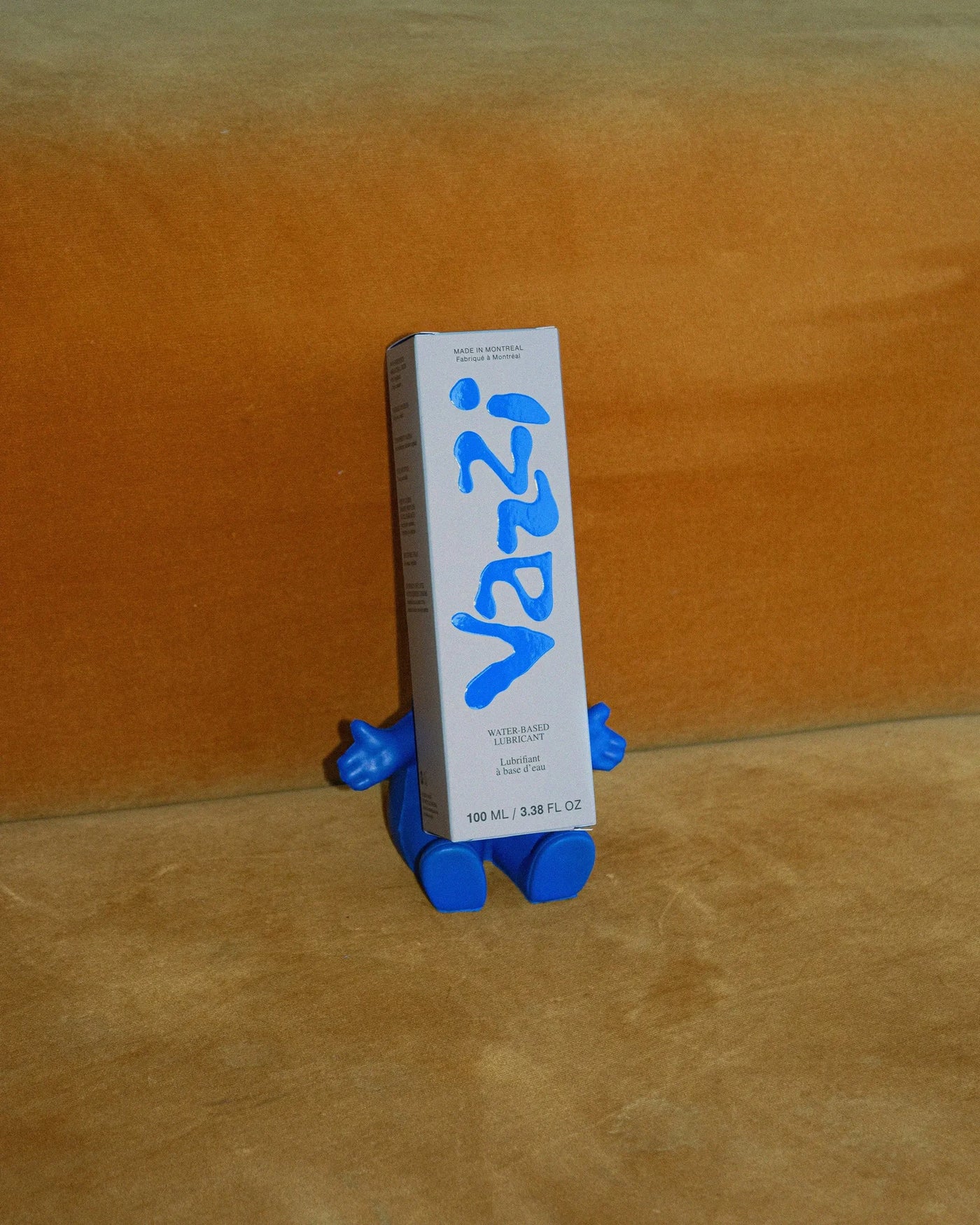 Vazzi — étui bleu et blanc maintenu par une petite figurine sur fond ocre