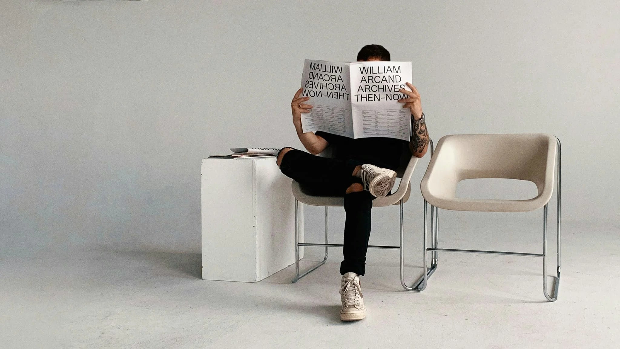 Then-Now — homme assis lisant le journal grand format au wordmark « William Arcand Archives Then-Now »