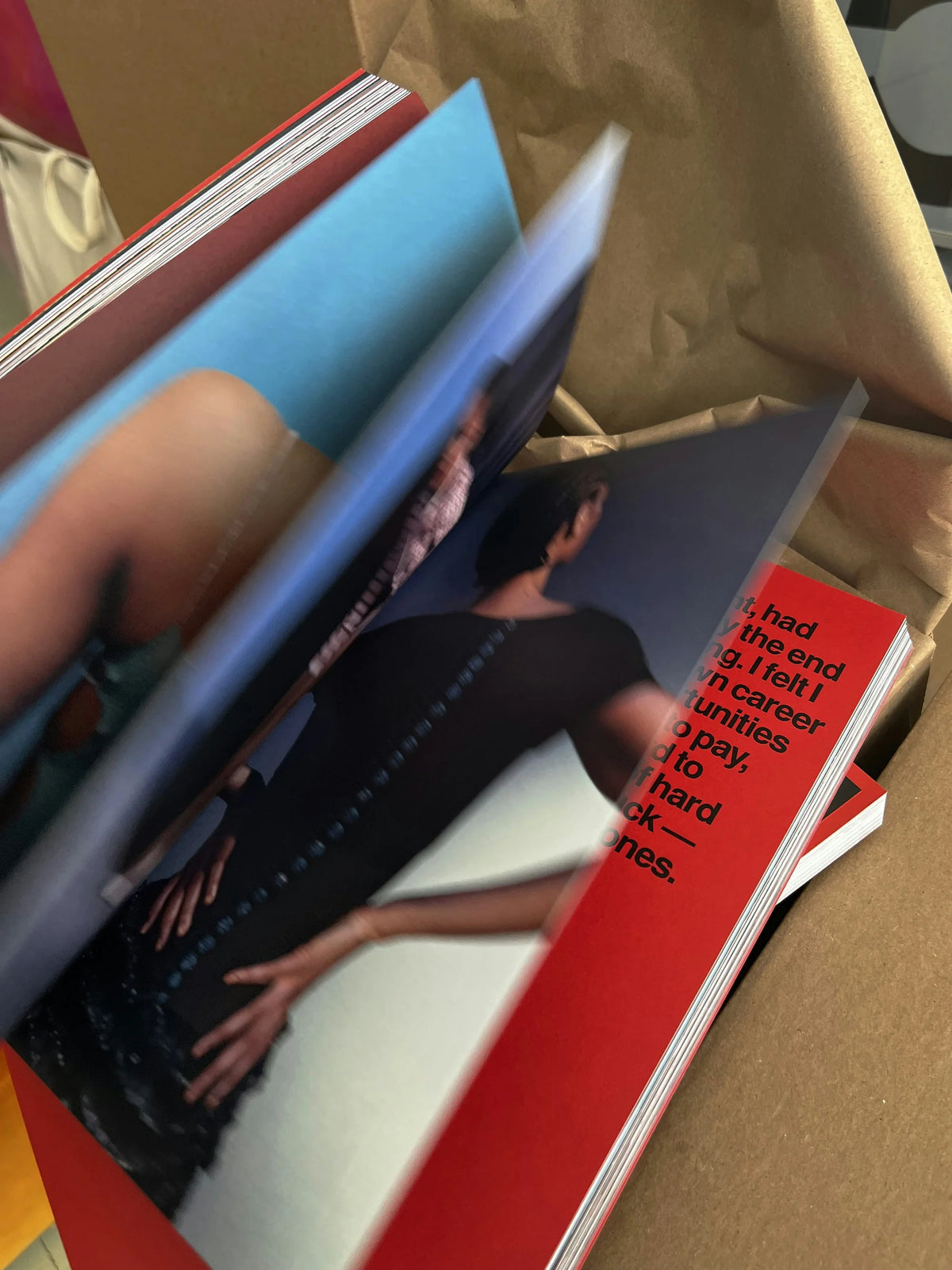 Now — exemplaires du livre dans un emballage ouvert, double-pages photo et texte rouge visibles